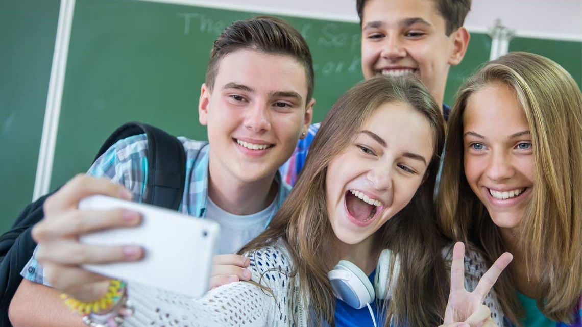 Vier Jugendliche in der Schule posieren vor einem Smartphone.