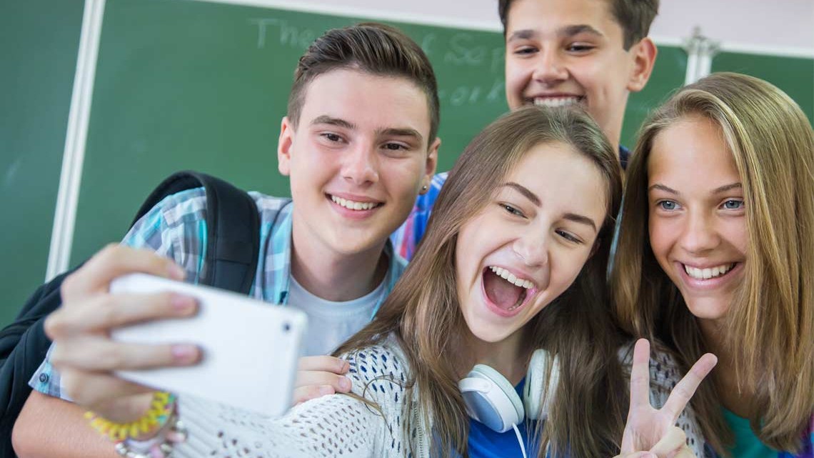 Vier Jugendliche in der Schule posieren vor einem Smartphone. Vier Jugendliche in der Schule posieren vor einem Smartphone.
